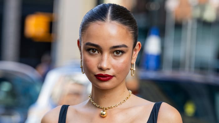 Kelsey Merrits poses in a black dress, gold chain necklace and drop earrings.